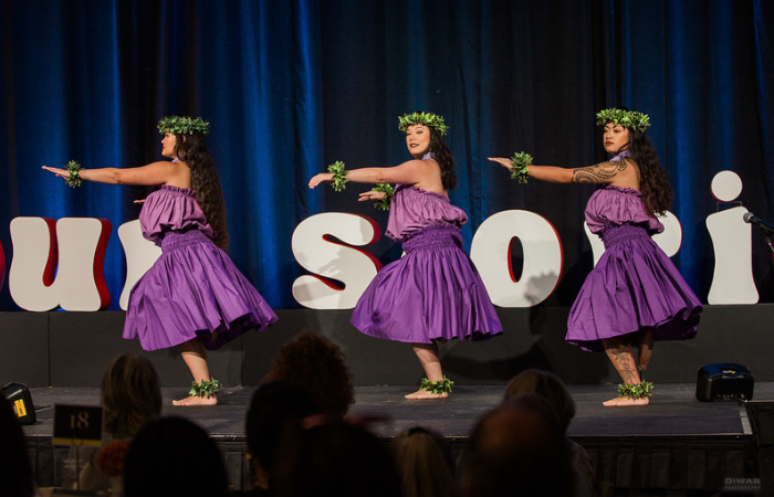 A photo of three hula dancers wearing purple clothes dancing on stage.