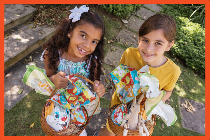 Two children looking up at the camera, holding easter baskets filled with goodies.