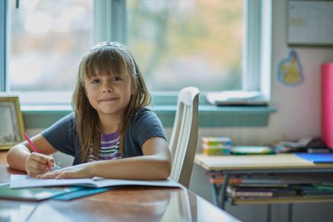 A young girl does her homework at the kitchen table.