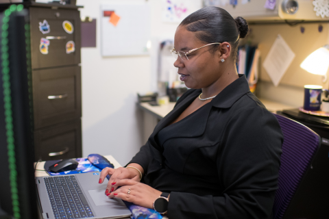 A side profile photo of Caprice Strange from the waist up sitting at a desk working on the computer.