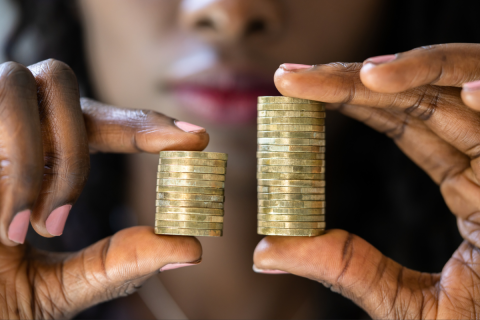 A photo of a black woman holding two stacks of coins up to the camera. The stack of coins on the left is smaller than the stack on the right.