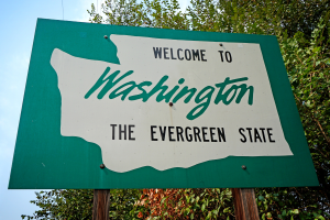 A photo of a sign with a white drawing of Washington State, reading "Welcome to Washington, the evergreen state"